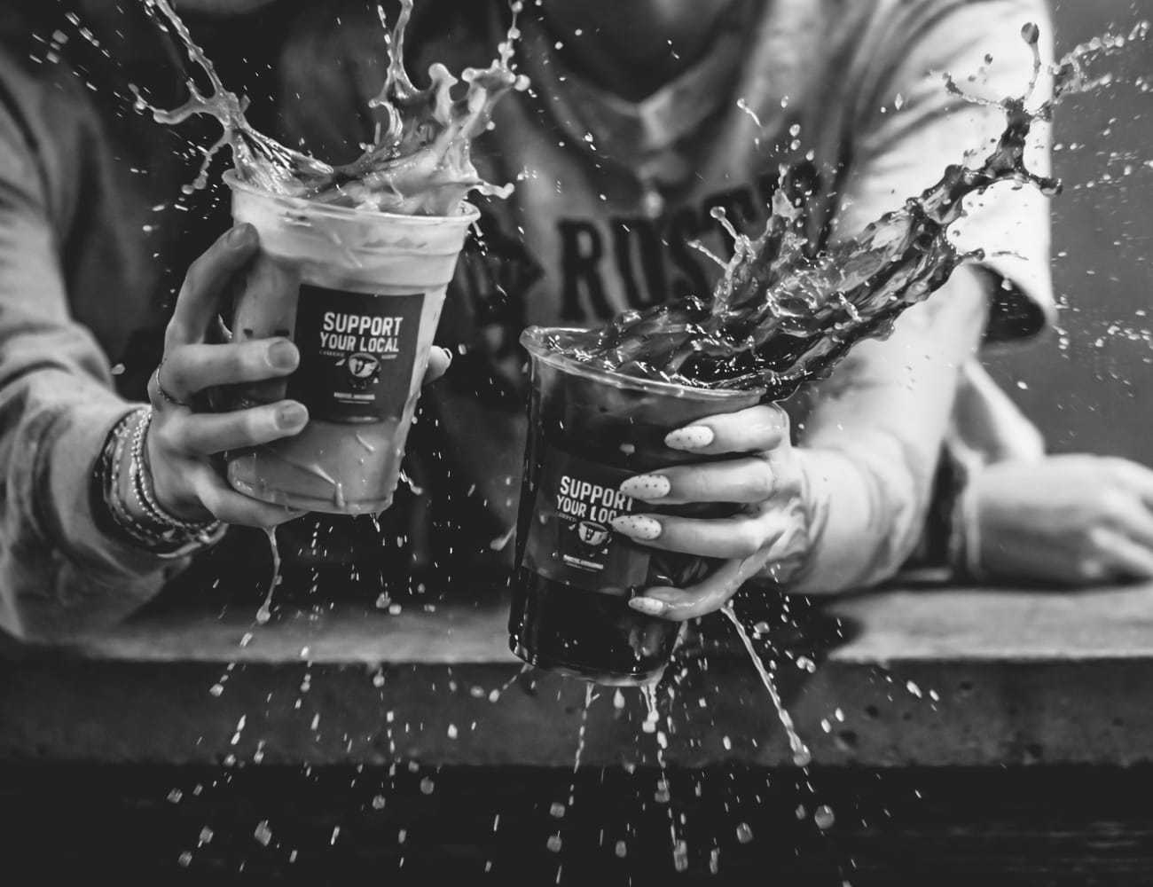 Two people joyfully clinking iced drinks with splashes captured in mid-air.