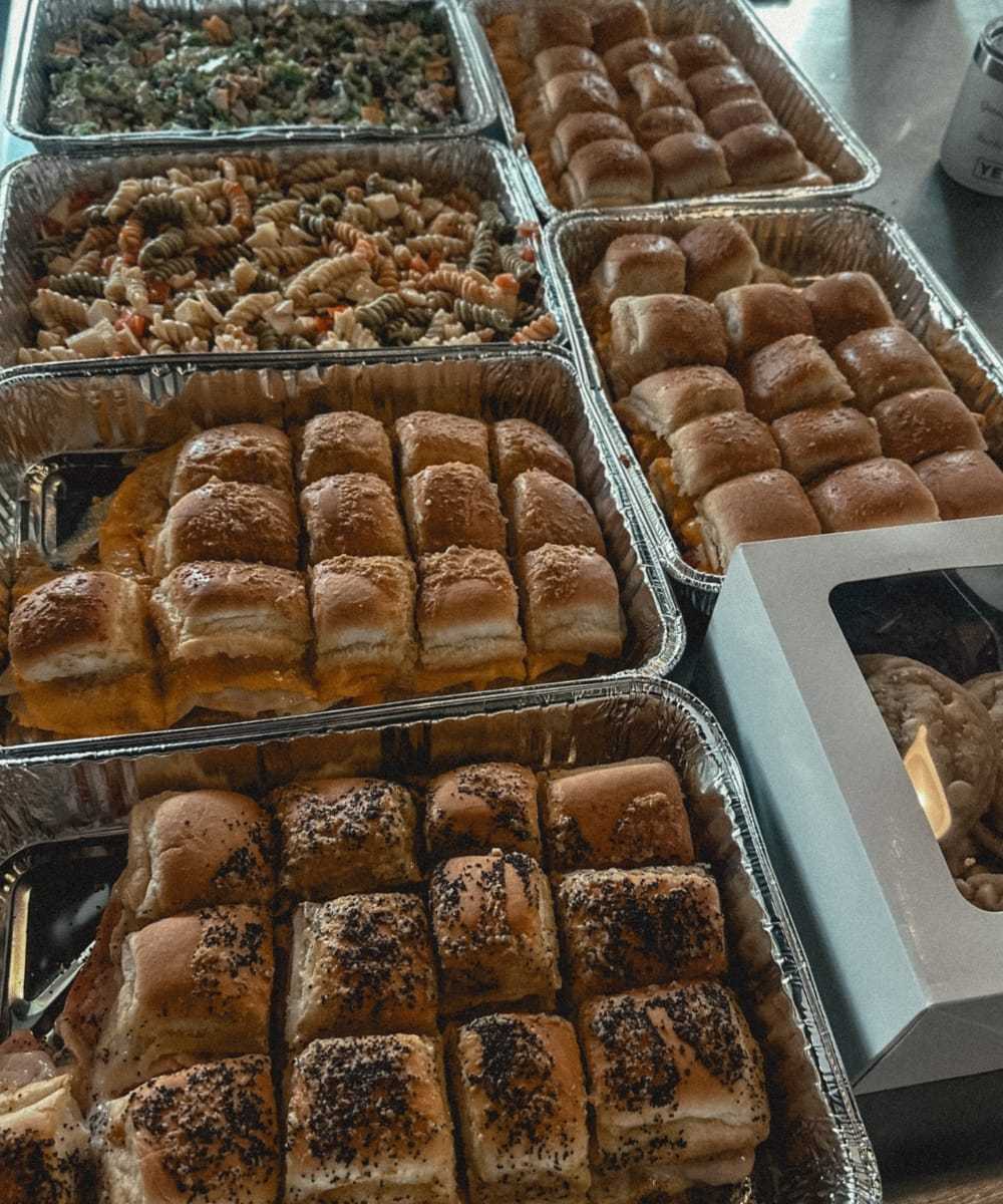 Buffet with trays of sandwiches, pasta salad, and cookies on a table.