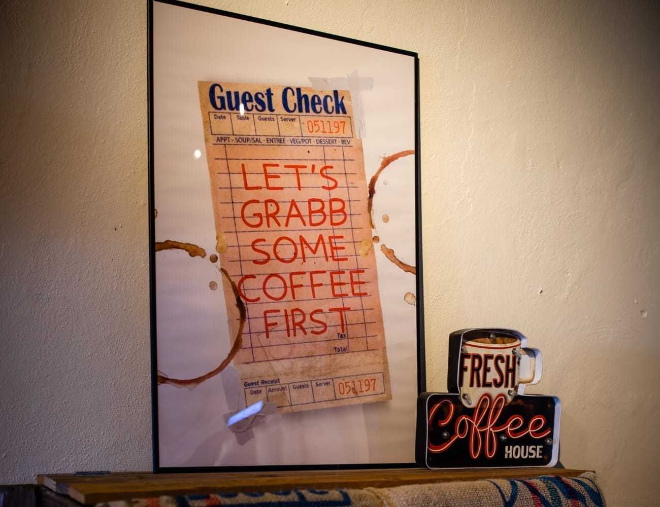 Framed coffee-themed artwork and mugs with coffee stains on a wall display.
